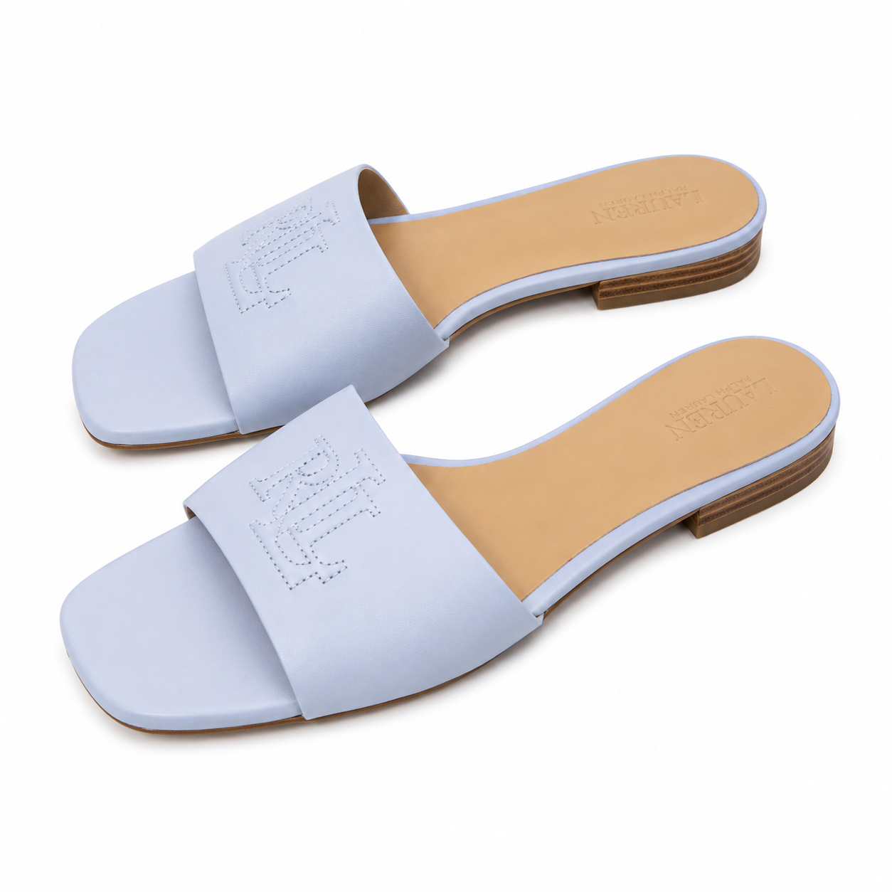 A pair of light blue leather slide sandals with square toes and a low stacked heel, featuring an embossed monogram on the strap and a tan insole.