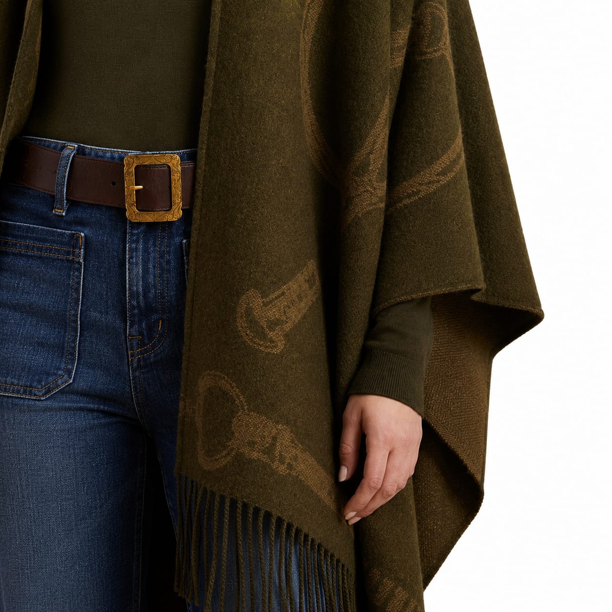 An olive green knit poncho with a subtle woven pattern and fringe hem, styled over an olive green top and blue jeans with a brown belt.