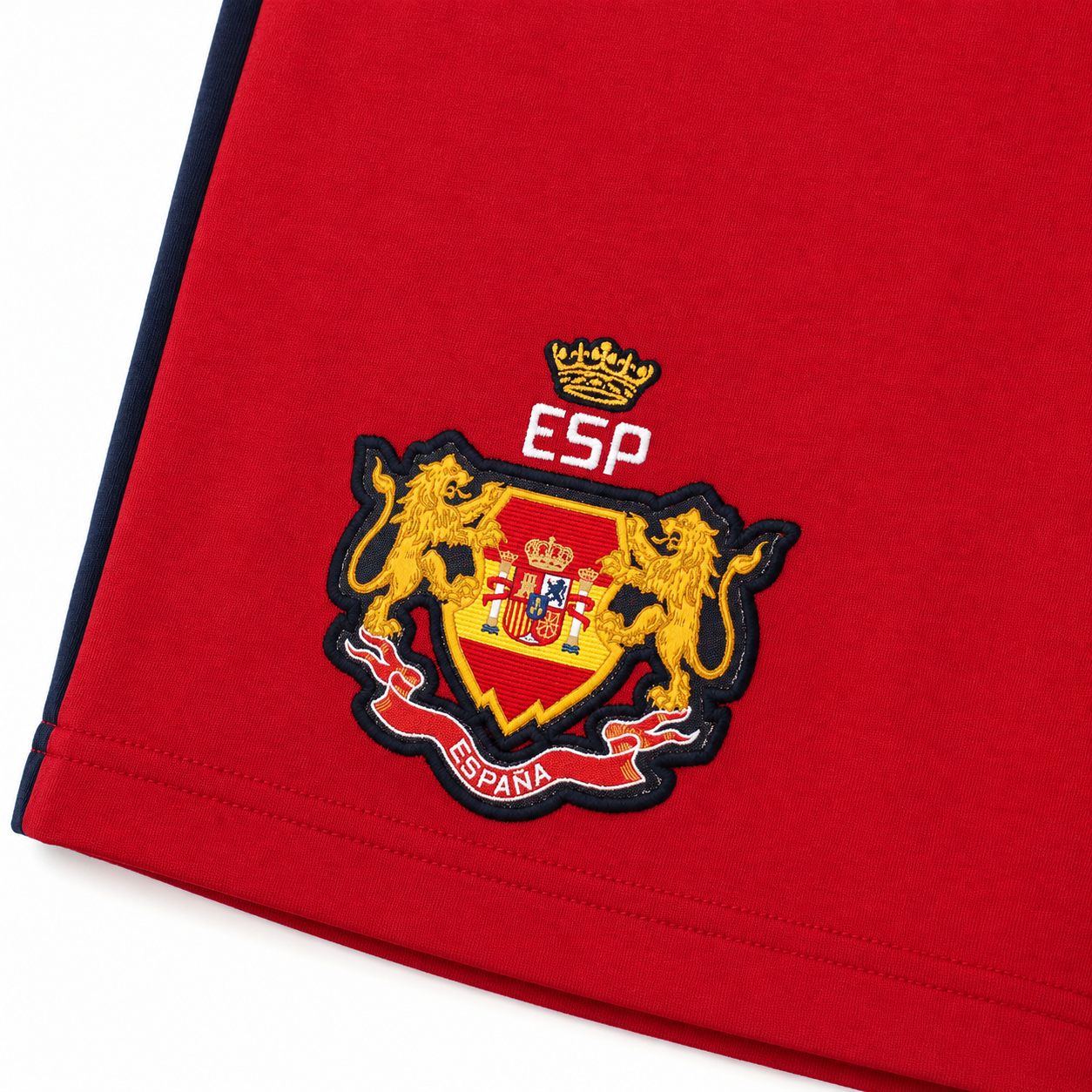 Close-up of a red Spain national team jersey showing the embroidered team crest with two golden lions, a crown, and the letters ESP on the chest.