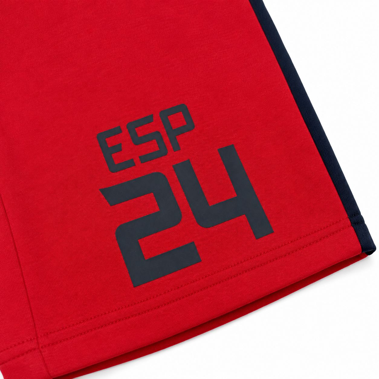 Close-up of a red garment corner with a dark navy 'ESP 24' graphic print and a dark navy edge trim, shown on a white background.
