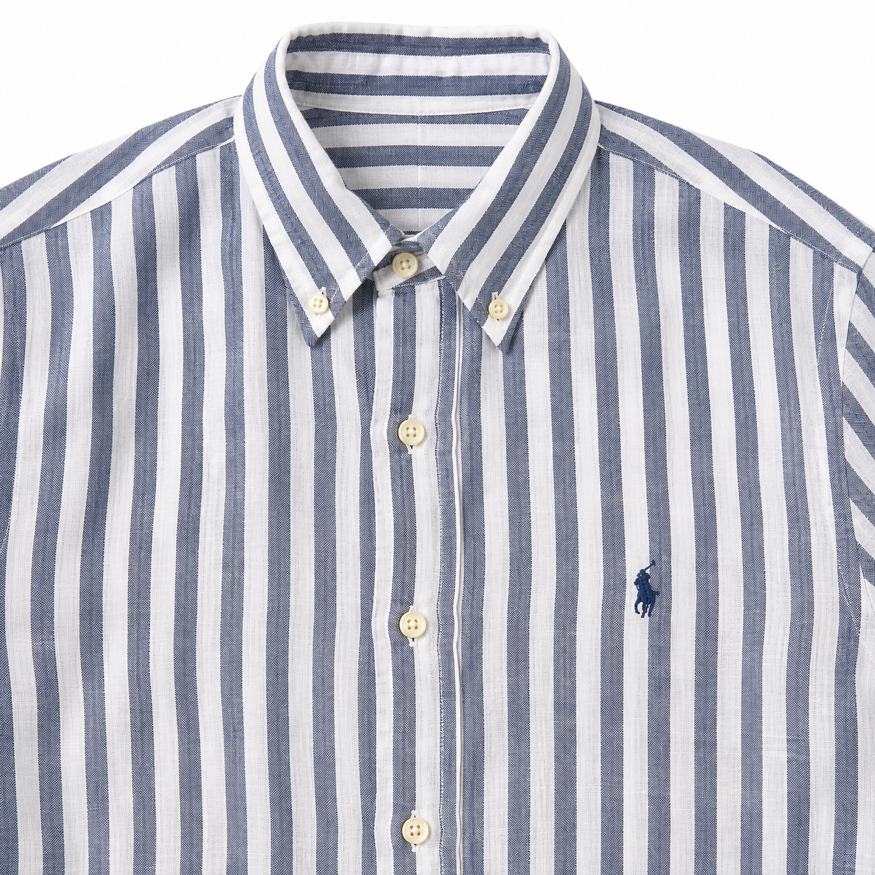 A close-up of a striped button-down shirt in white and navy blue, featuring a small navy blue embroidered polo player logo on the chest.
