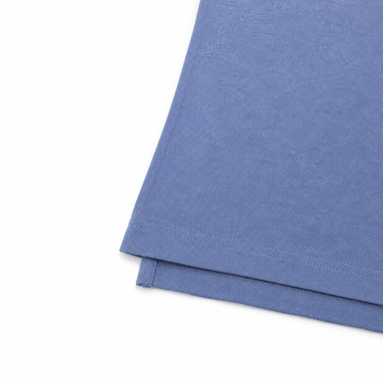 A close-up of folded blue fabric with a fine knit texture, showing a hemmed edge, on a plain white background.
