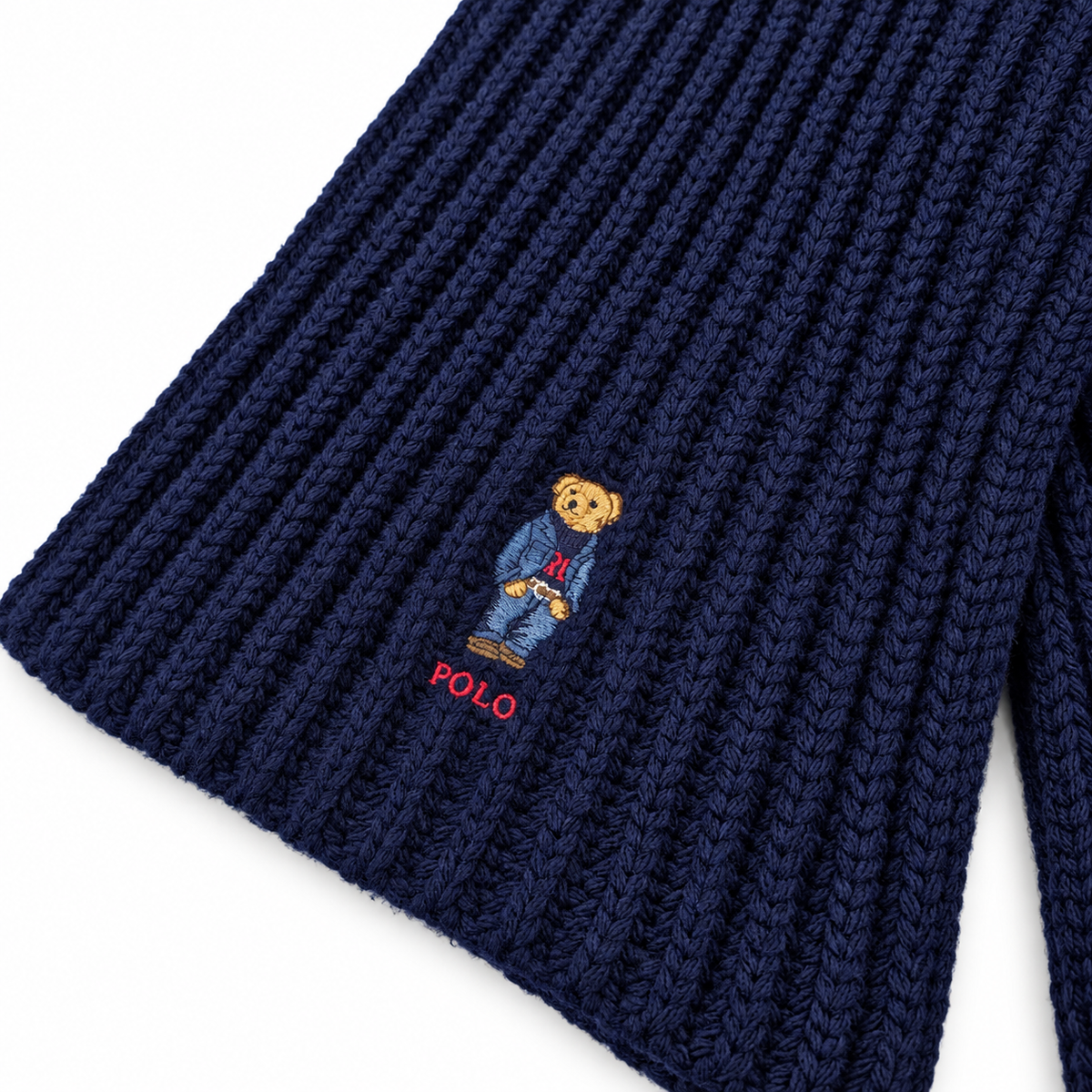 Close-up of a navy blue ribbed knit garment, likely a beanie or sweater cuff, featuring the embroidered Polo Bear logo and the word 'POLO' in red on a white background.