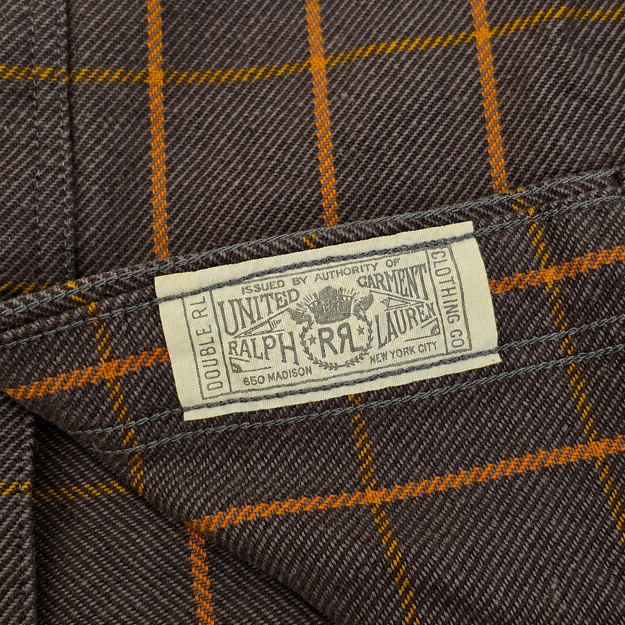 Close-up of a brown plaid fabric with orange windowpane lines and a visible United Ralph Lauren label sewn into the inside of the garment.