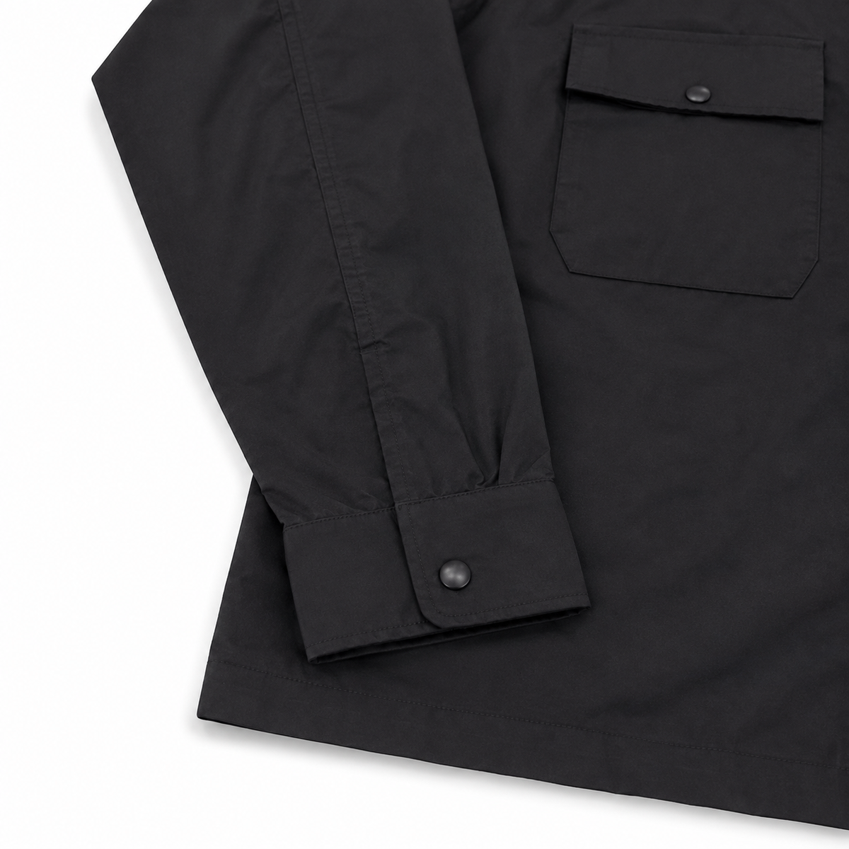 Close-up of a black long-sleeve utility jacket showing the sleeve cuff with a snap button and a chest pocket with a snap closure, set against a plain white background.
