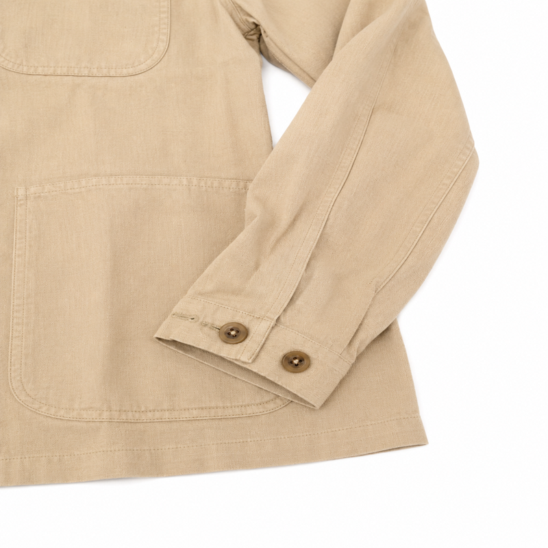 Close-up of a beige canvas utility jacket with a chest pocket and a buttoned cuff, shown on a white background.