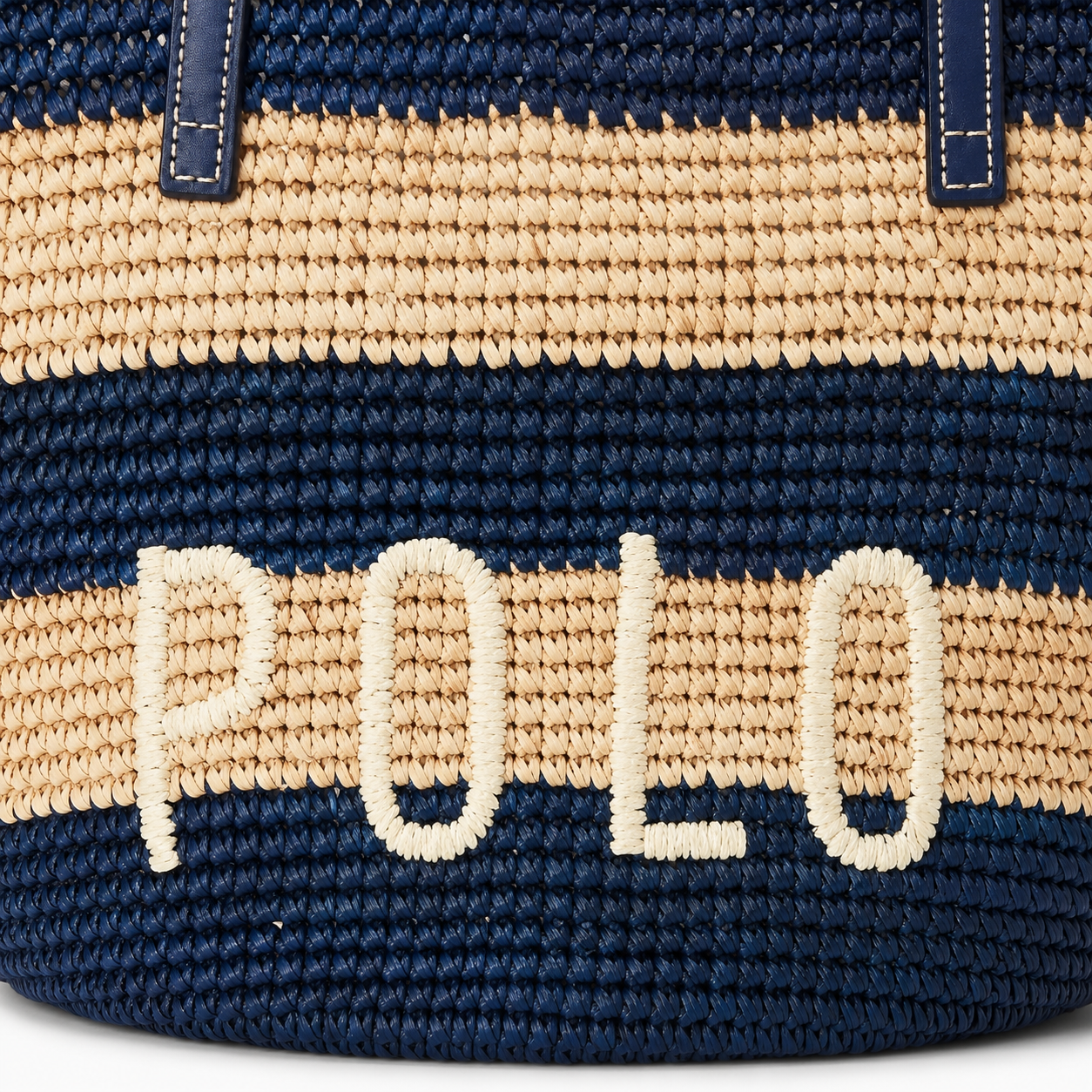 Close-up of a woven straw bag with navy blue and beige horizontal stripes, featuring the embroidered white text 'POLO' and dark blue strap tabs.