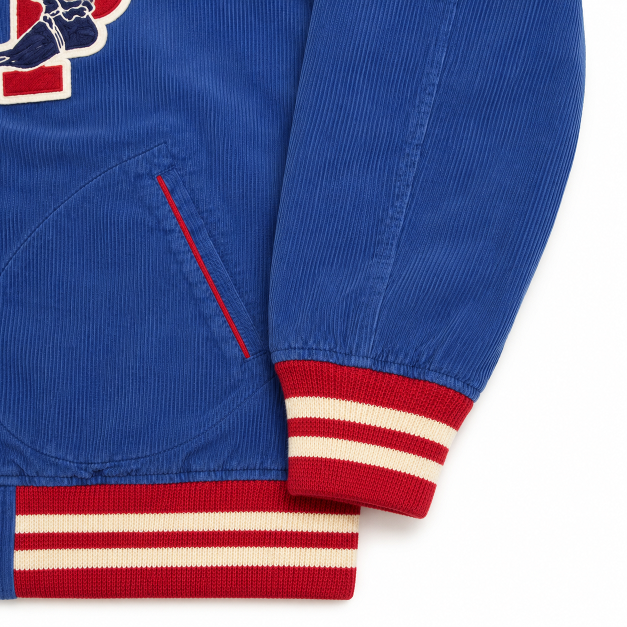 Close-up of a royal blue corduroy jacket with red and cream striped ribbed cuffs and a red accent line near a pocket, on a white background.