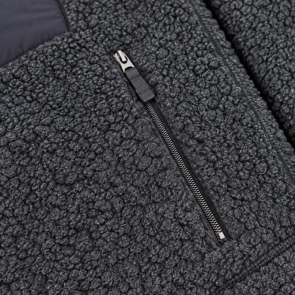 Close-up of a dark gray sherpa fleece jacket with a black zipper and silver metal pull.