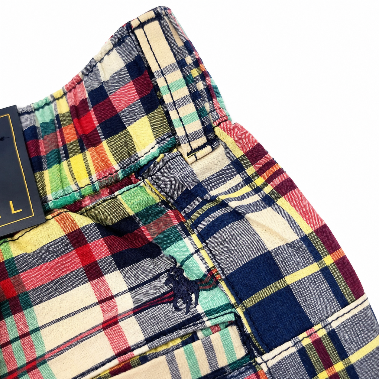 Close-up of a plaid pair of shorts showing the waistband, belt loops, pocket, and a small embroidered polo player logo on a white background.