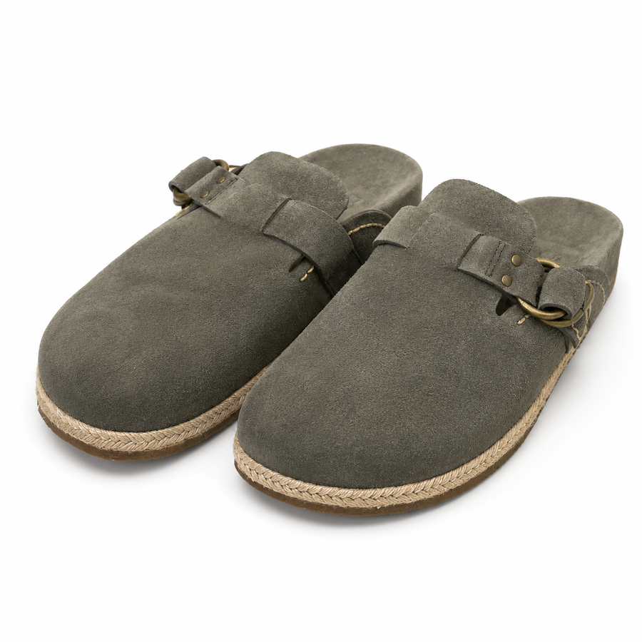 A pair of dark gray suede mule clogs with braided jute soles and brass-tone buckle straps, shown on a clean white background.