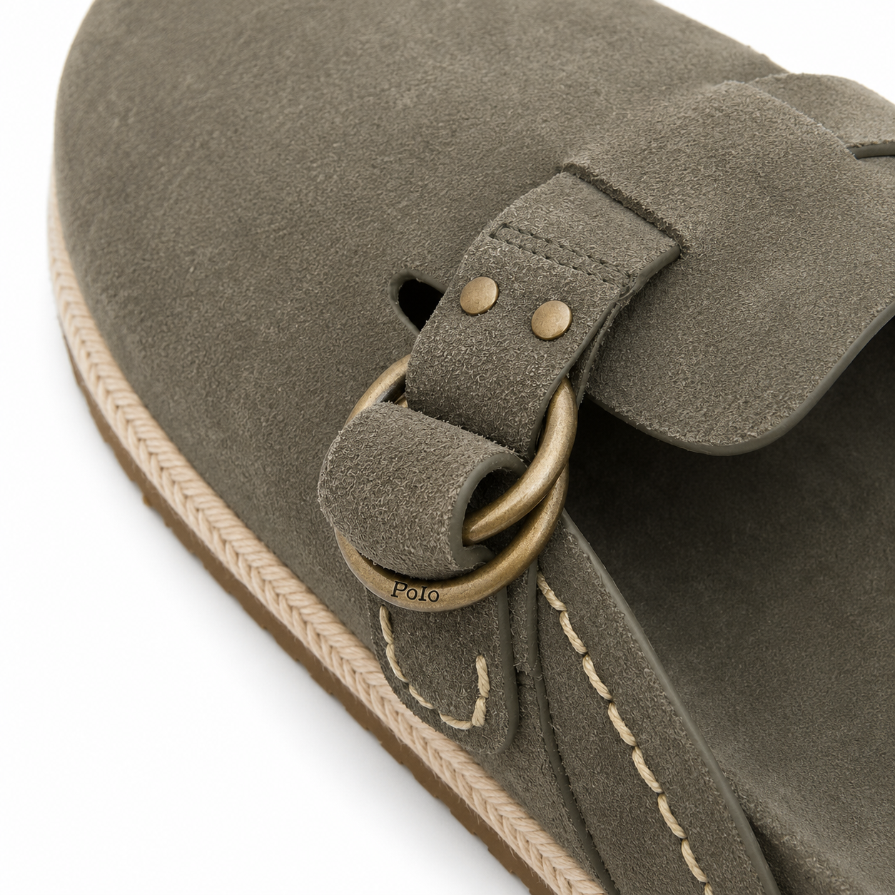 Close-up of a taupe suede clog shoe by Polo Ralph Lauren, showing the strap, brass-tone O-ring, stitching, and braided sole edge on a white background.