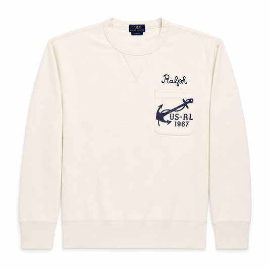 An off-white crewneck sweatshirt by Polo Ralph Lauren featuring a chest pocket with a navy blue anchor logo and 'US-RL 1967' text.