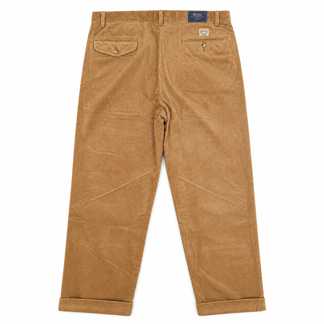 A pair of tan corduroy trousers shown from the back, featuring two buttoned flap pockets and a blue brand label at the waistband, laid flat on a white background.