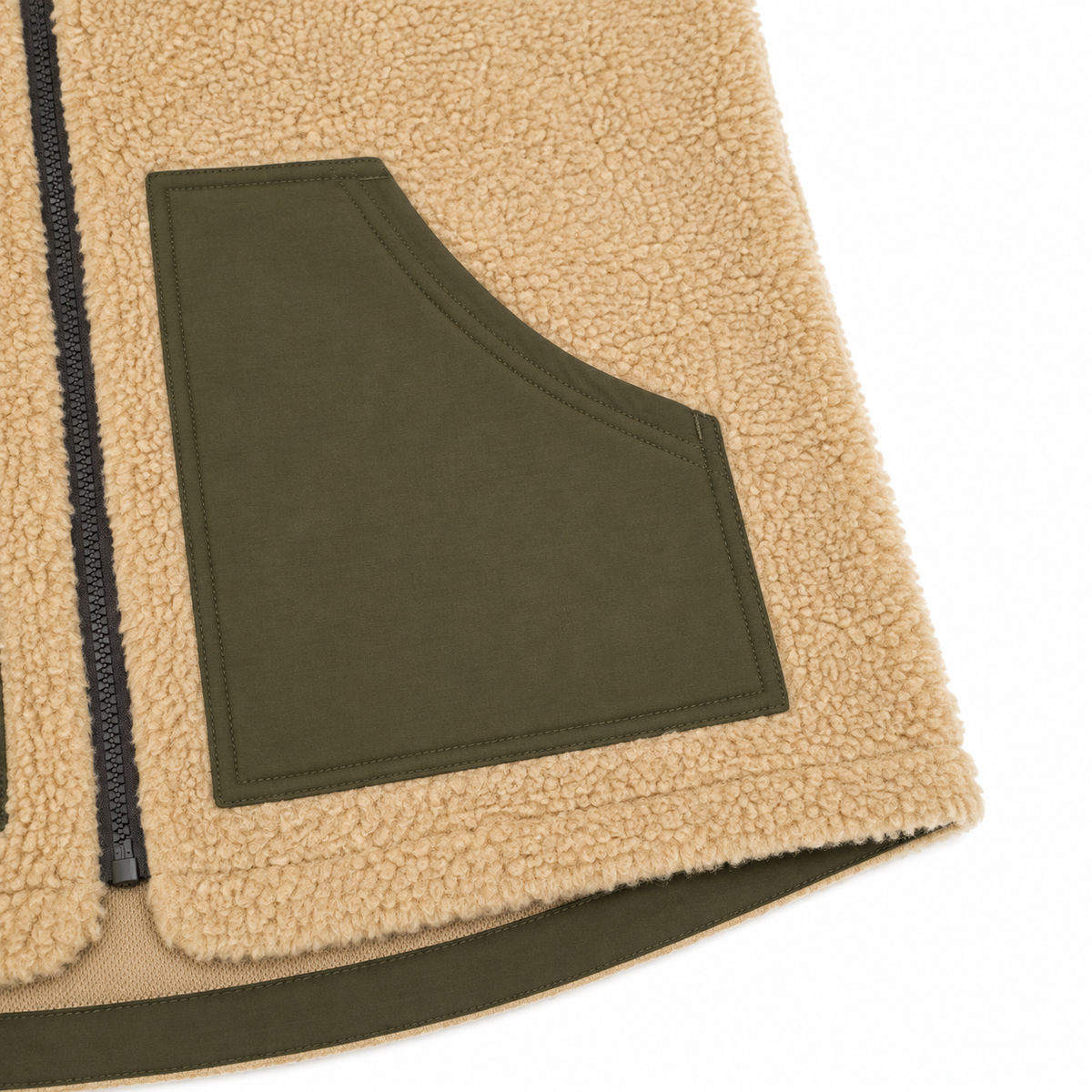 Close-up detail of a fleece jacket showing a tan sherpa fabric body, an olive green patch pocket, and a black zipper on a white background.