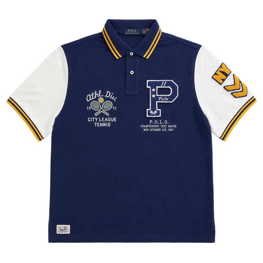 A navy blue and white Polo Ralph Lauren short-sleeve polo shirt with yellow and navy striped accents on the collar, cuffs, and sleeves, featuring tennis-themed graphics on the chest.