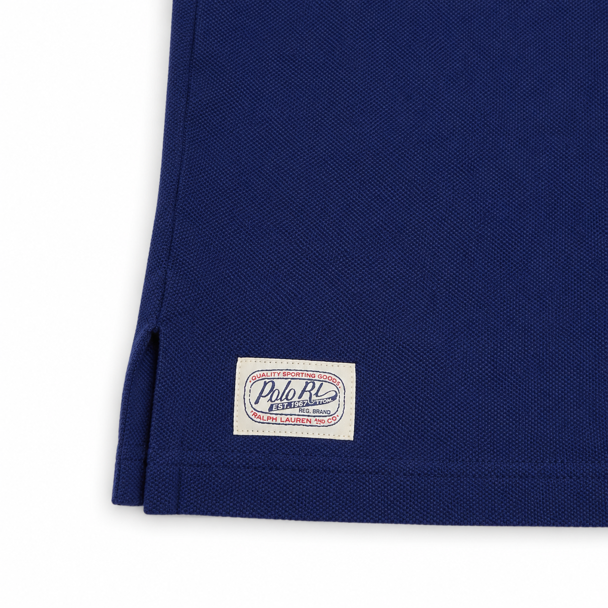Close-up of a navy blue polo shirt corner showing a white Polo Ralph Lauren woven label on the hem.
