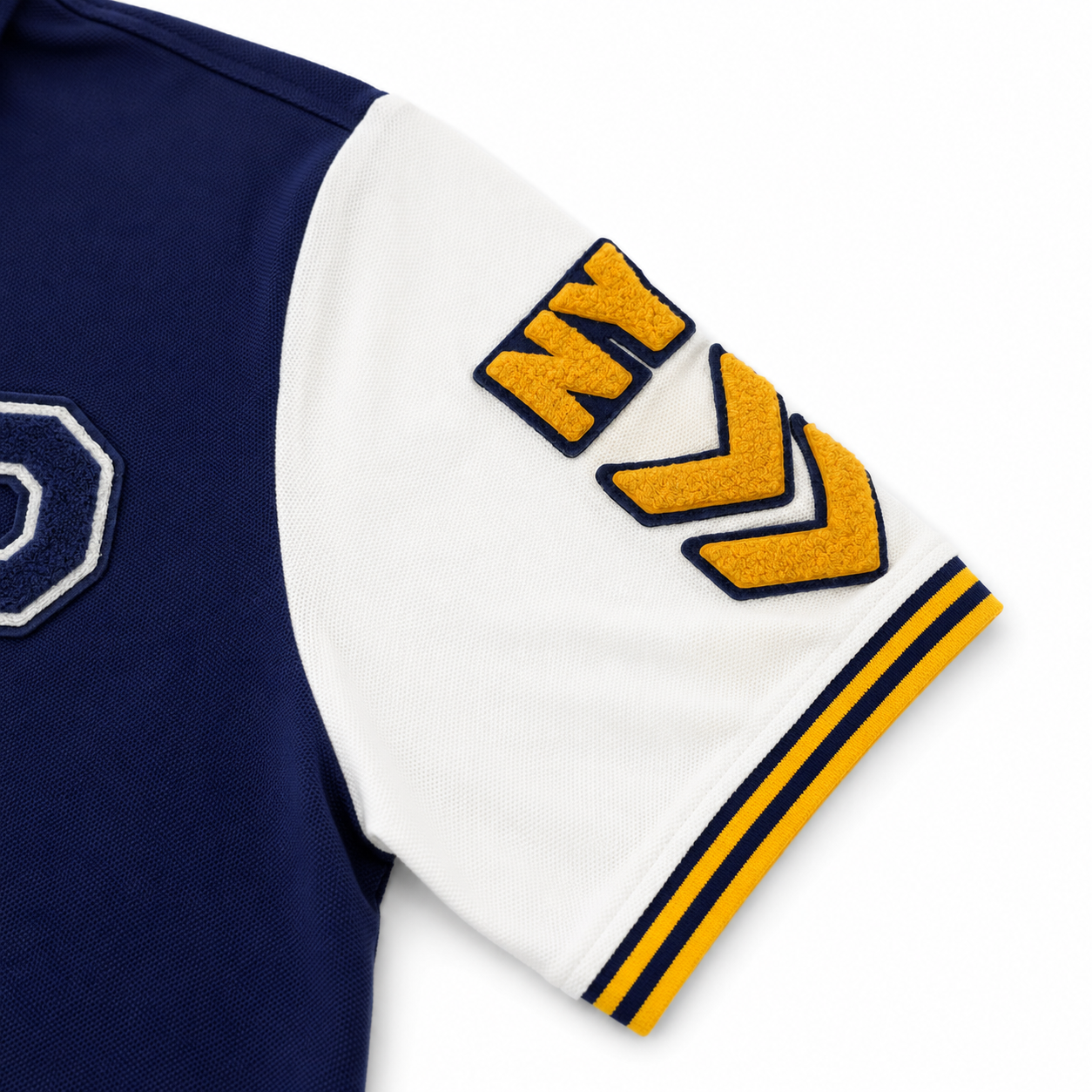 Close-up of a navy and white athletic jersey sleeve featuring a large yellow and navy embroidered 'NY' patch on the white shoulder area and yellow-and-navy striped ribbing at the cuff.